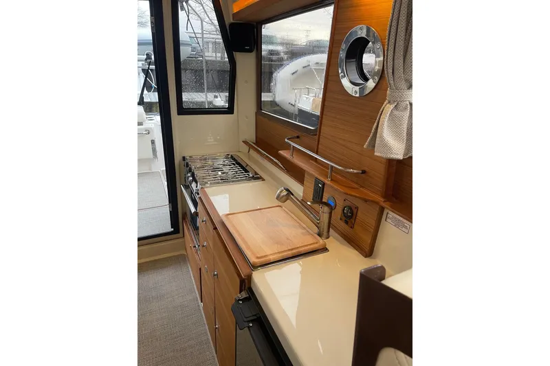 Slide: The Image of 2026 Ranger Tug R-27 interior kitchen with stove, sink, and window view. - 7