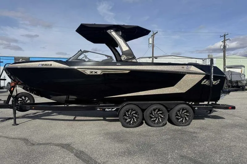 Slide: The Image of 2025 Tigé Ultré 25ZX boat on trailer, sleek black design, parked outdoors. - 2