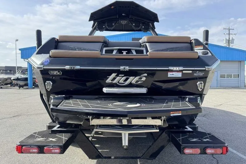 Slide: The Image of 2025 Tigé Ultré 25ZX boat, rear view, black exterior, parked near blue building. - 7