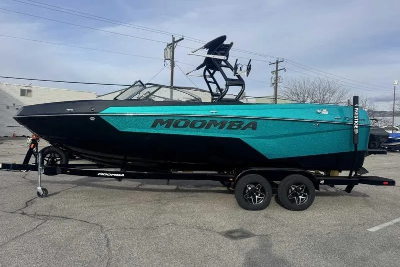 Slide: The Image of 2026 Moomba Tykon boat on trailer, vibrant teal and black design, parked outdoors. - 2
