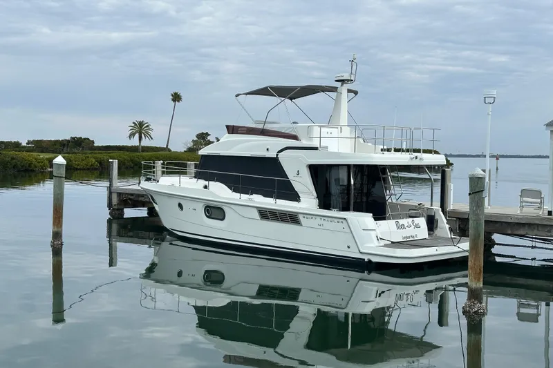 Slide: The Image of 2021 Beneteau Swift Trawler 41 Fly docked on calm water, with palm trees in the background. - 1