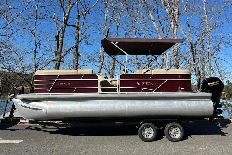 Slide: The Image of 2022 Godfrey Sweetwater 2286 C pontoon boat on trailer, parked near trees. - 4