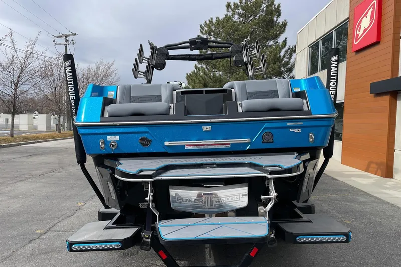 Slide: The Image of 2024 Malibu Wakesetter 26 LSV boat, blue exterior, parked outdoors near a building. - 4