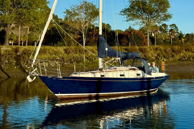Slide: The Image of Sailboat Contessa 32 from 1990 on calm water, surrounded by trees. - 1