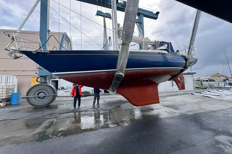Slide: The Image of 1990 Contessa 32 sailboat lifted in shipyard, blue hull, red keel, overcast sky. - 33