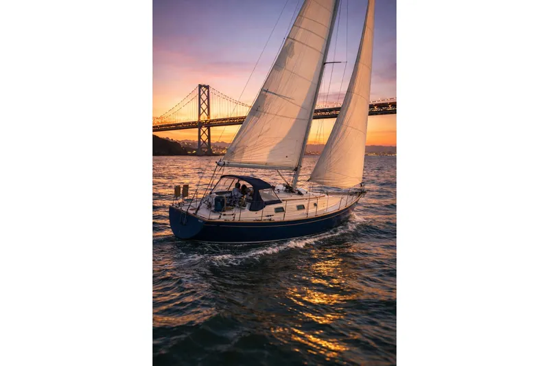 Slide: The Image of Sailboat Contessa 32 (1990) cruising at sunset near a bridge, reflecting on water. - 35