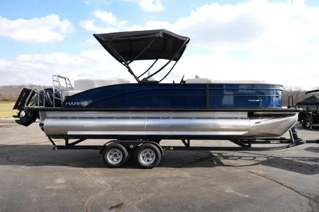 Slide: The Image of 2026 Harris Cruiser 230 pontoon boat with canopy on a trailer, parked outdoors. - 10