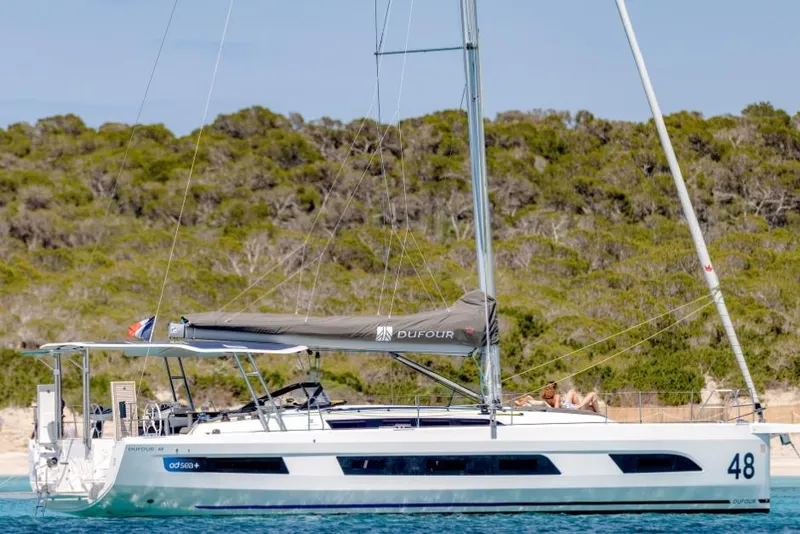Slide: The Image of 2026 Dufour 48 yacht sailing near a lush, green coastline. - 3