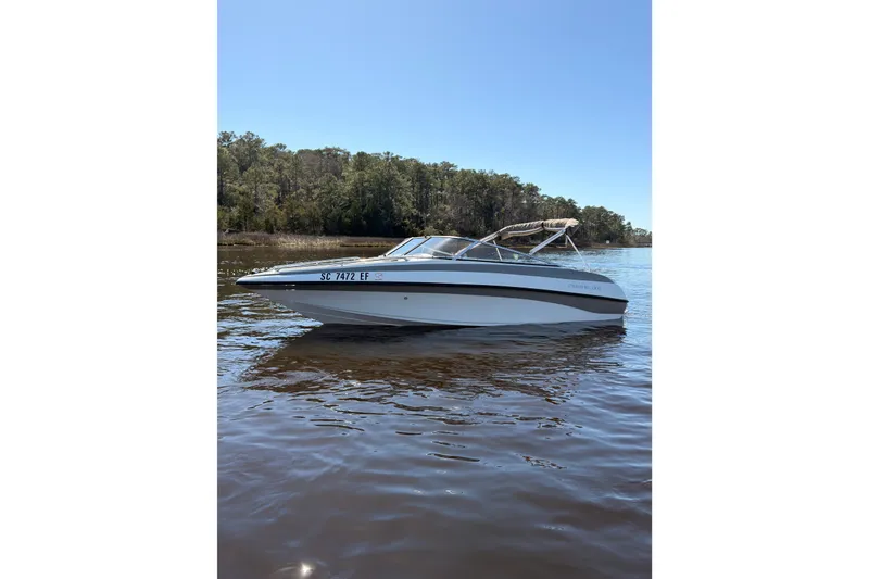Slide: The Image of 2003 Crownline 180 BR boat on calm water with forested shoreline. - 2