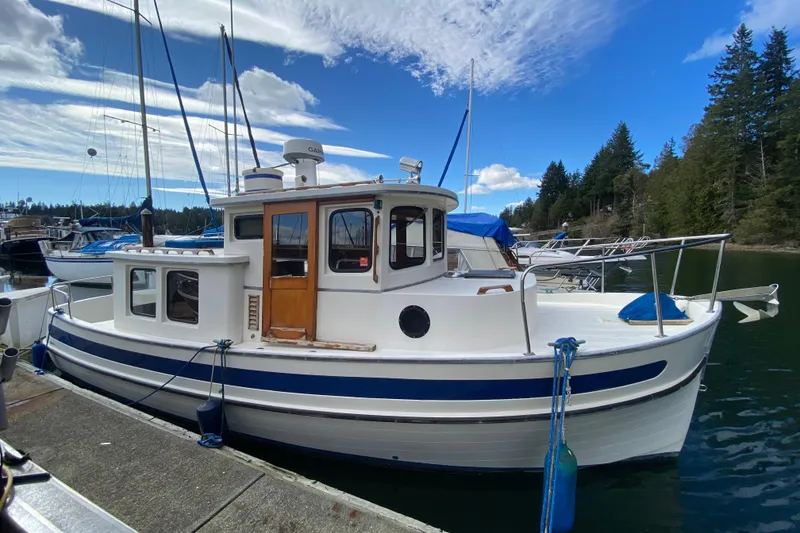 The Image of 1988 Nordic Tug 26 docked at a marina, surrounded by trees and blue sky. - 0