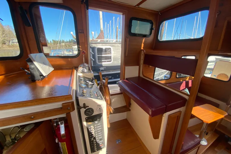 Slide: The Image of 1988 Nordic Tug 26 interior with wooden helm, seating, and marina view. - 16