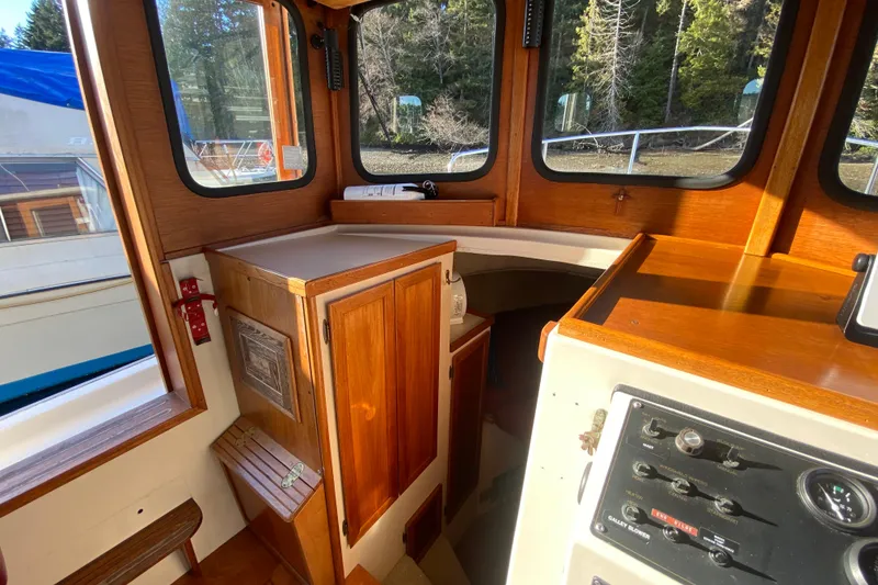 Slide: The Image of 1988 Nordic Tug 26 interior with wooden cabinetry and control panel, forest view outside. - 17