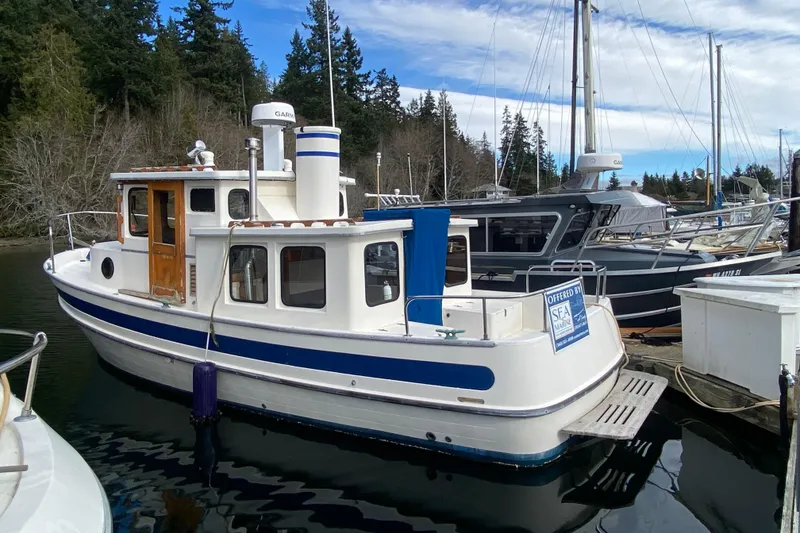 Slide: The Image of 1988 Nordic Tug 26 docked, featuring classic design and blue accents, surrounded by other boats. - 2