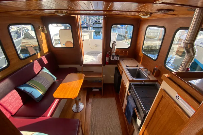 Slide: The Image of 1988 Nordic Tug 26 interior with cozy seating, wooden table, and compact kitchen area. - 22