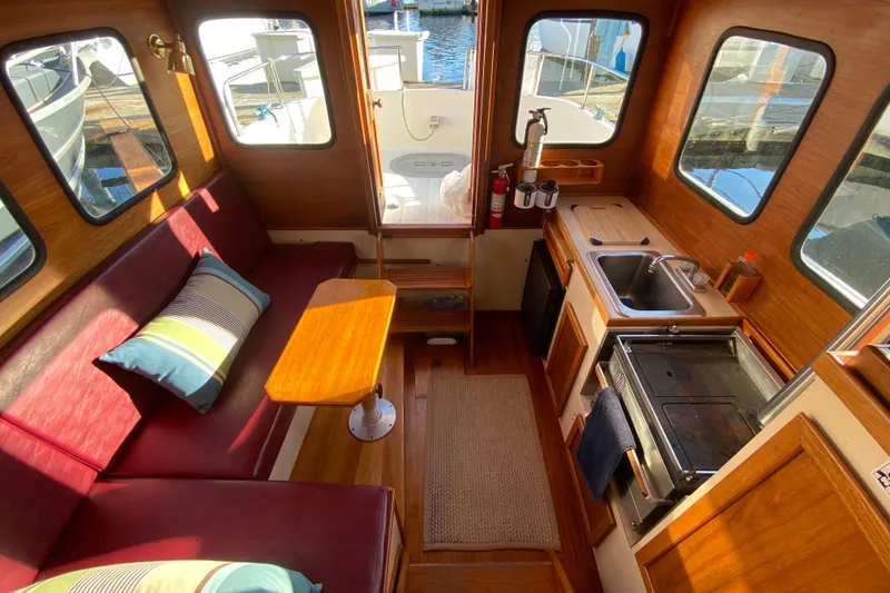 Slide: The Image of 1988 Nordic Tug 26 interior with cozy seating, wooden table, and compact kitchen area. - 24