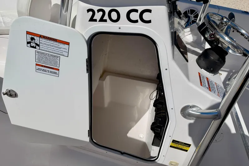 Slide: The Image of 2023 Aquasport 2200 Center Console storage compartment with open door and safety warnings. - 26