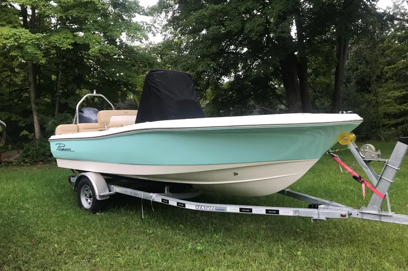 Slide: The Image of 2026 Pioneer 180 Islander boat on trailer, parked on grass with trees in background. - 2
