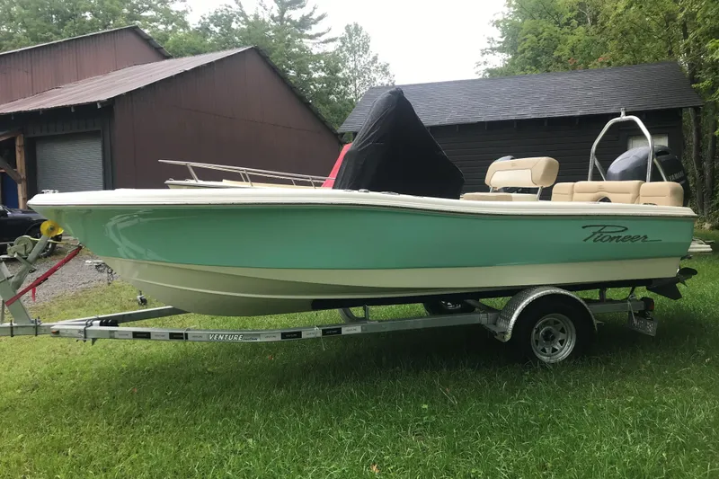 Slide: The Image of 2026 Pioneer 180 Islander boat on trailer, parked on grass near a barn. - 7