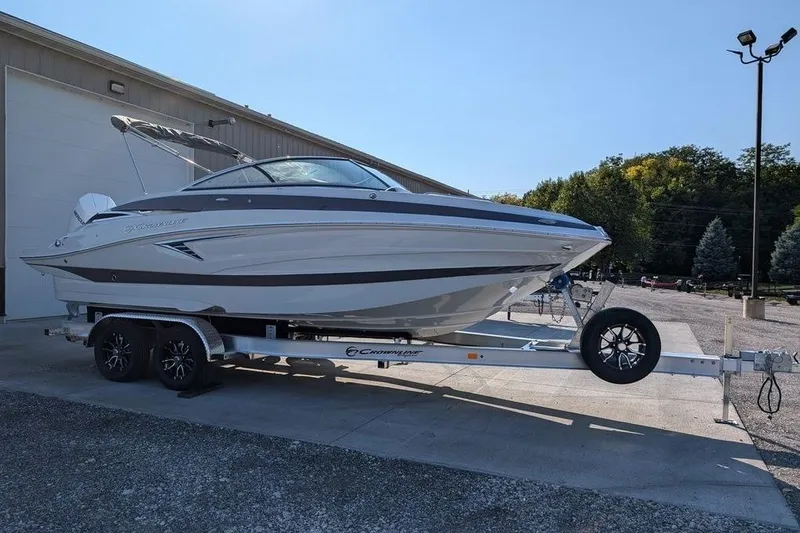 The Image of 2024 Crownline Eclipse E240 XS boat on trailer, parked outdoors near a building. - 0