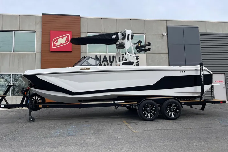 The Image of 2026 Nautique Super Air Nautique GS24 boat on trailer outside dealership. - 1