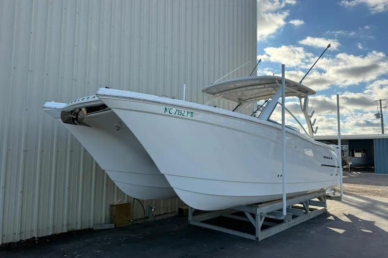 The Image of 2024 World Cat 280 DC-X boat on a trailer, parked beside a building under a partly cloudy sky. - 1