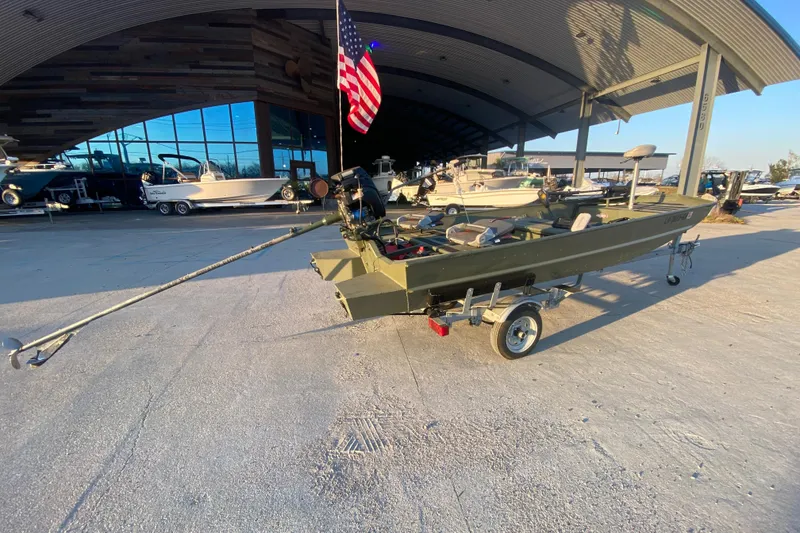 Slide: The Image of 2012 Alumacraft 1448 Jon boat on trailer, displayed outdoors with American flag. - 3