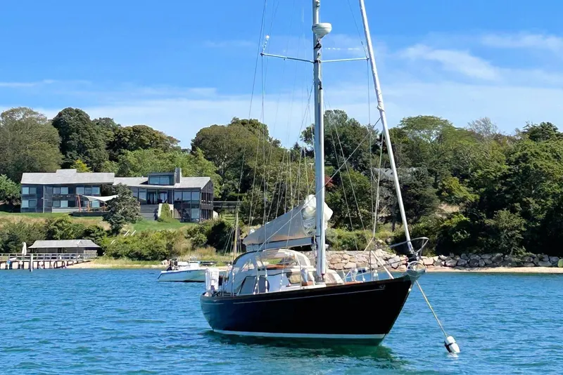 Slide: The Image of 1967 Columbia Constellation sailboat anchored near a scenic shoreline with modern houses. - 9
