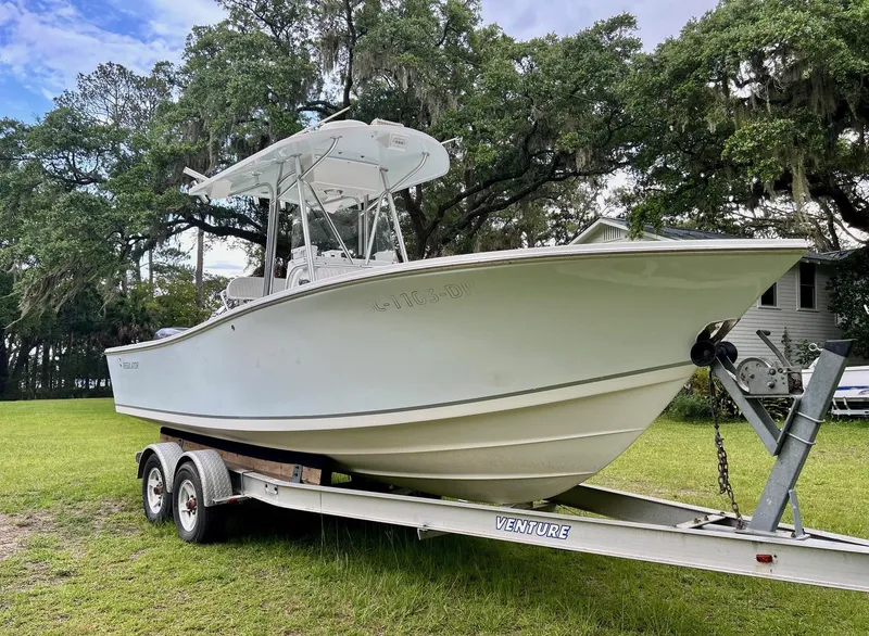 The Image of 2000 Regulator 23' Center Console boat on trailer, parked on grass with trees in background. - 0