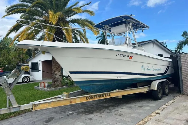 Slide: The Image of 1997 Cobia 244 Center Console boat on trailer, parked near palm trees and house. - 1