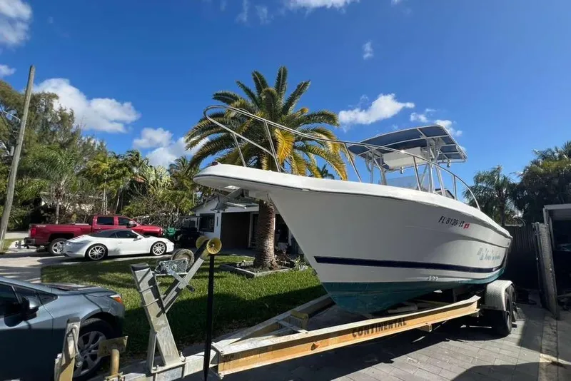 Slide: The Image of 1997 Cobia 244 Center Console boat on trailer, parked in sunny residential area. - 2