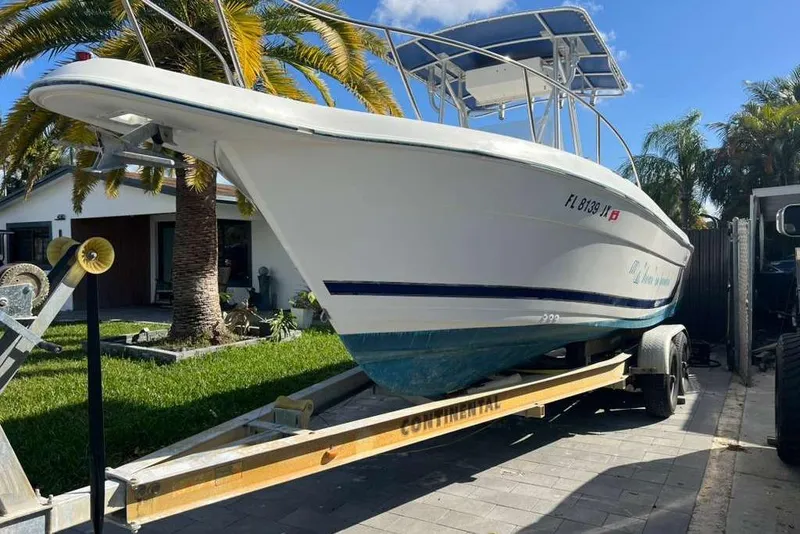 Slide: The Image of 1997 Cobia 244 Center Console boat on trailer, parked in driveway with palm trees. - 4