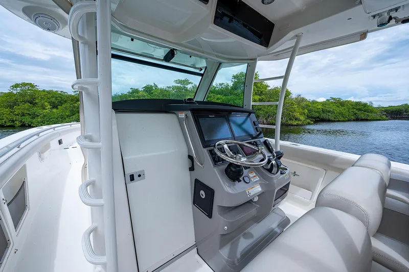 Slide: The Image of 2017 Boston Whaler 370 Outrage helm with modern controls, near lush shoreline. - 33