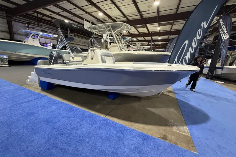 Slide: The Image of 2026 Pioneer 180 Islander boat displayed indoors on blue carpet at a boat show. - 1