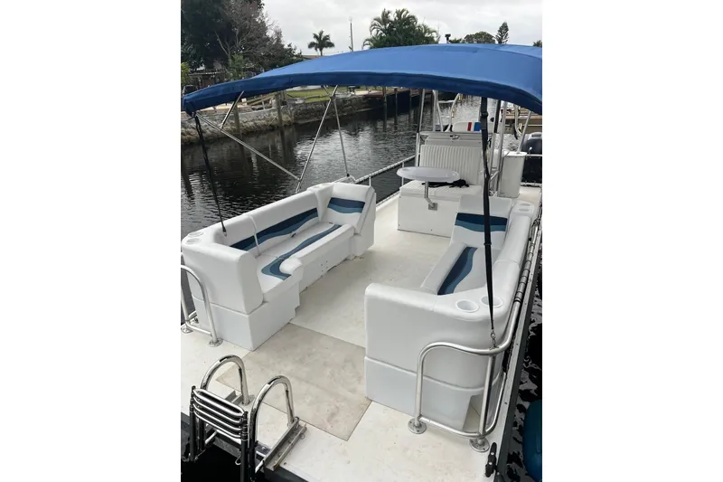 Slide: The Image of 2010 A&M Manufacturing Triton Pontoon with blue canopy and white seating on a calm waterway. - 4