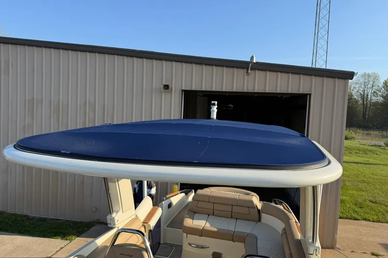 Slide: The Image of 2025 Chris-Craft Launch 28 GT boat with blue canopy, parked near a metal building. - 42