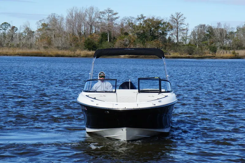 Slide: The Image of 2025 Searay SPX210 boat cruising on a serene lake with a scenic forest backdrop. - 12