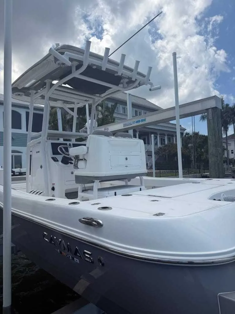 Slide: The Image of A modern Caymas 26 HB boat with T-top and helm console, set against a waterfront house. - 1