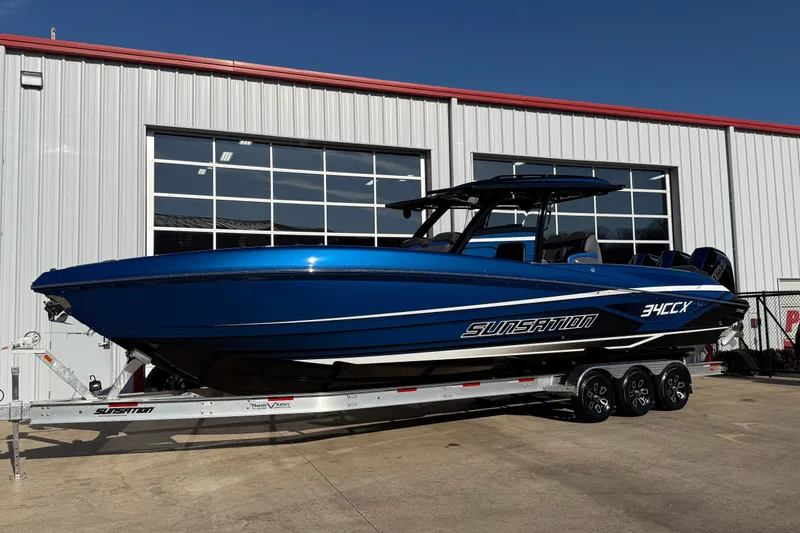 Slide: The Image of 2026 Sunsation 34 CCX boat in vibrant blue on a trailer outside a building. - 4