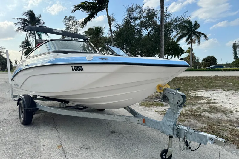Slide: The Image of 2025 Yamaha Boats SX190 on trailer, parked near palm trees under a blue sky. - 1