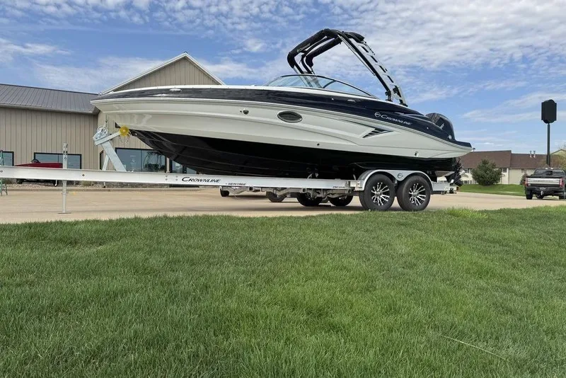 Slide: The Image of 2025 Crownline 250 XSS boat on trailer, parked on grass, under a partly cloudy sky. - 12