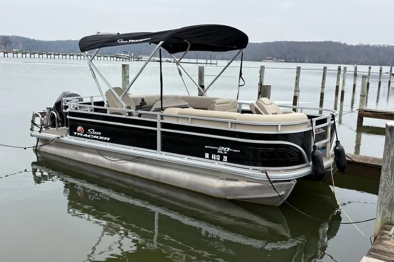 The Image of 2024 Sun Tracker SportFish 20 DLX pontoon boat docked on a calm lake. - 0