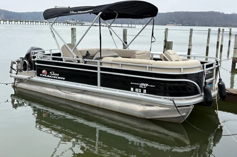 Slide: The Image of 2024 Sun Tracker SportFish 20 DLX pontoon boat docked on a calm lake. - 2