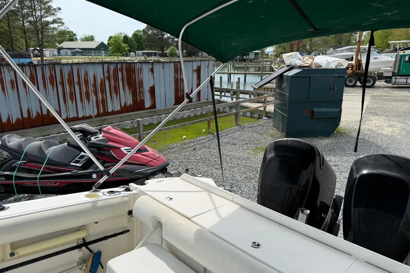 Slide: The Image of 2006 Trophy 2502 Walkaround boat with dual engines, docked near jet skis and a rusted fence. - 8