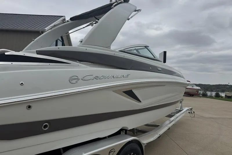 Slide: The Image of 2025 Crownline 270 XSS boat on trailer, parked outdoors under cloudy sky. - 2