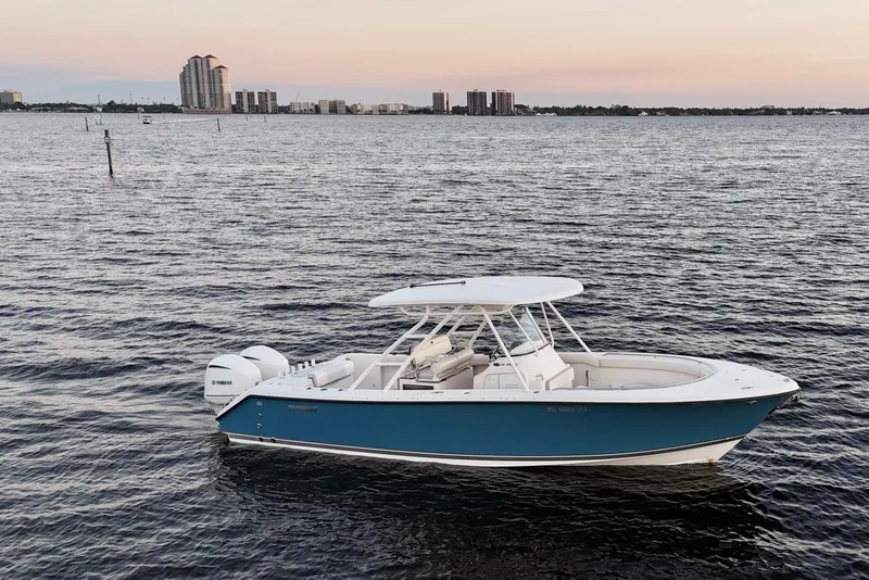 Slide: The Image of 2014 Pursuit S 280 Sport boat on calm water at sunset, city skyline in background. - 7
