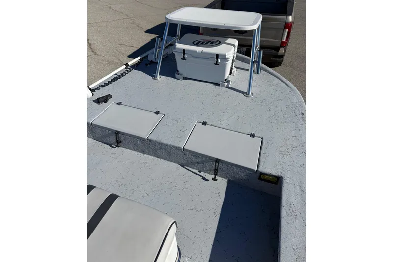 Slide: The Image of 2006 Shoalwater 21 Cat boat deck with seating and cooler, parked on pavement. - 11