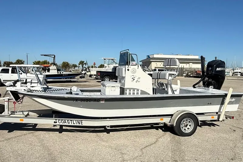 Slide: The Image of 2006 Shoalwater 21 Cat boat on trailer, parked in marina lot under clear blue sky. - 1
