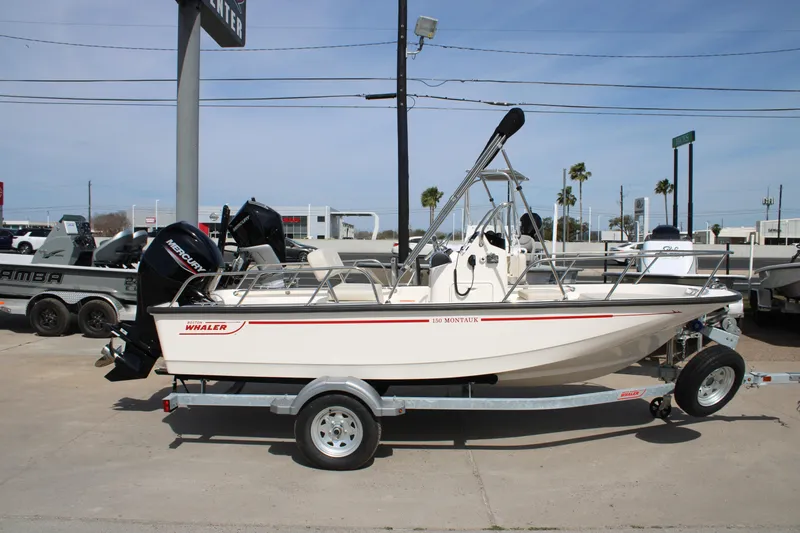 Slide: The Image of 2026 Boston Whaler 150 Montauk boat on trailer, displayed outdoors at dealership. - 2