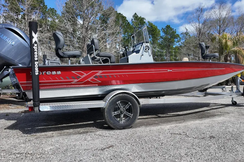 Slide: The Image of 2026 Xpress H22B Bay boat in red on a trailer, parked outdoors. - 2
