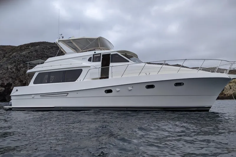 The Image of 2000 McKinna 48 Pilothouse yacht on water, overcast sky, rocky shoreline background. - 0